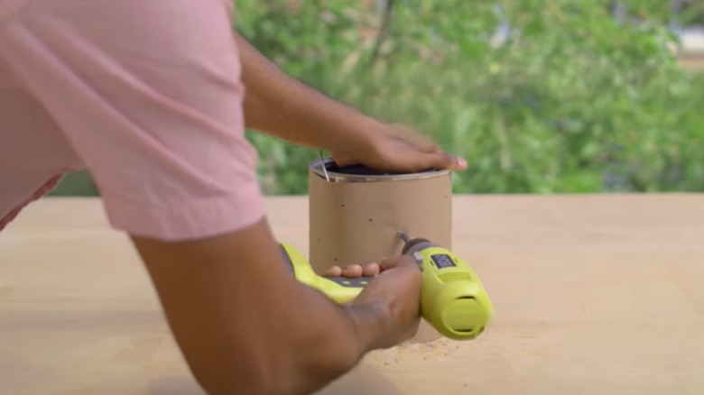 Person drilling holes into paint can to make DIY lantern