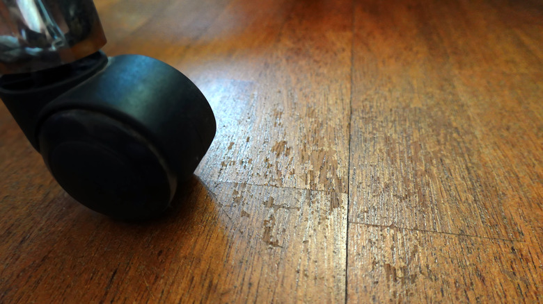 Wooden floor with visible signs of wear and damage caused by the wheels of office chair
