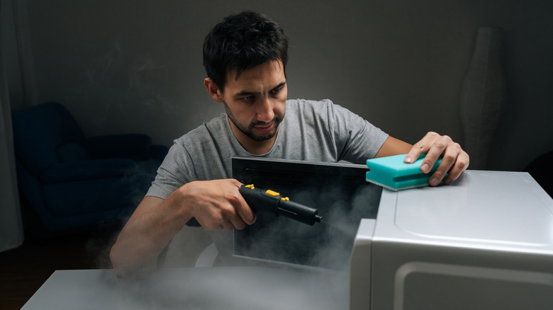 Person cleaning a microwave using a steamcleaner