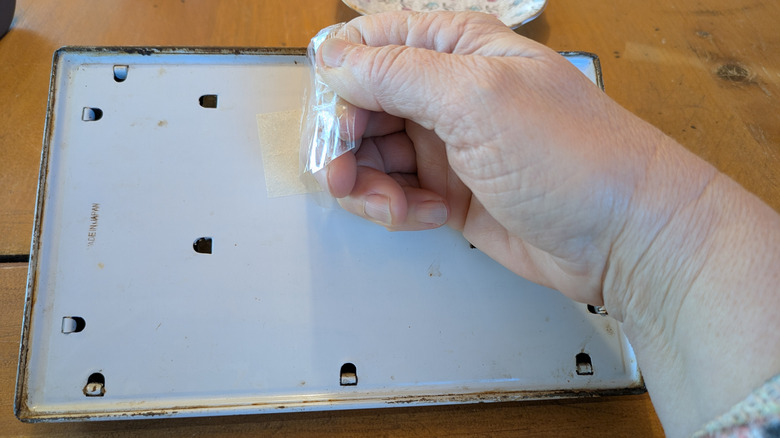 A hand pulls tape off a damaged price tag sticker on a metal item.