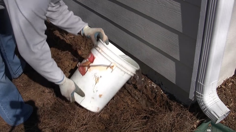 Man pouring a bucket of termiticide in a trench outside his house
