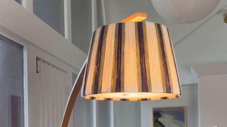 Lampshade wrapped around in cotton string in a striped pattern with cream, navy, and green colors