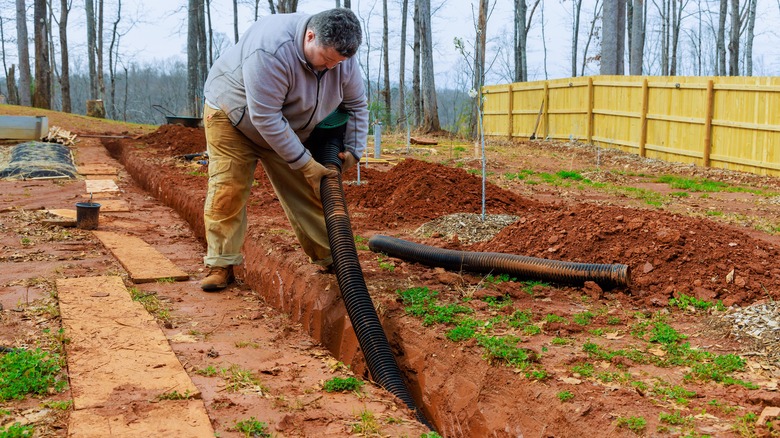 person laying underground downspout extension pipe