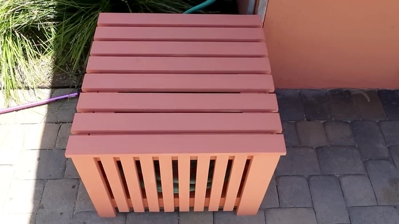 An orange DIY container with a green hose inside sits on a driveway