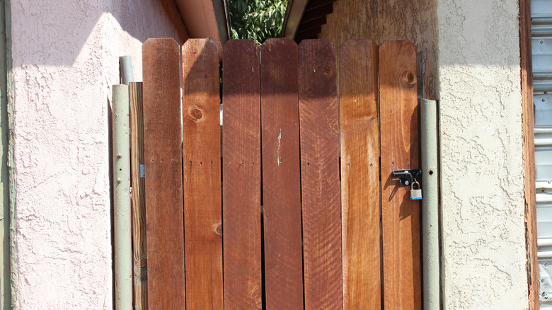 A DIY latching gate made of brown-stained timber fitted across the side of a house.