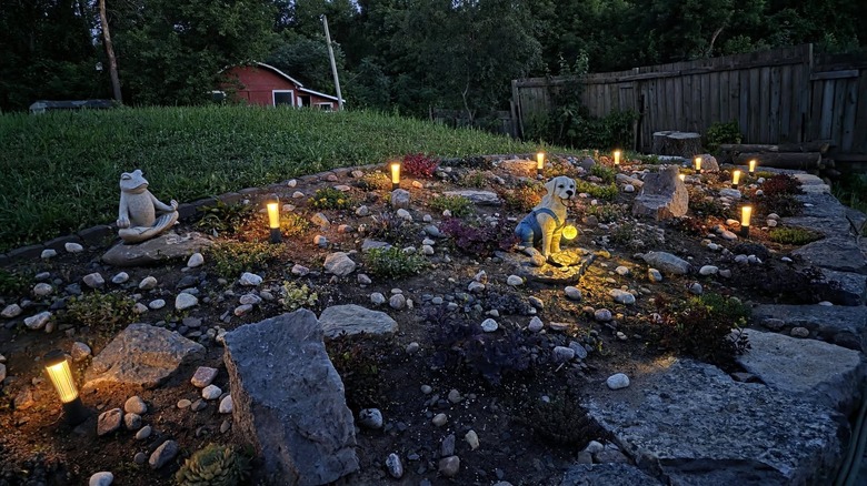 A backyard with a DIY rock garden including statues, lights, small stones, and larger rocks