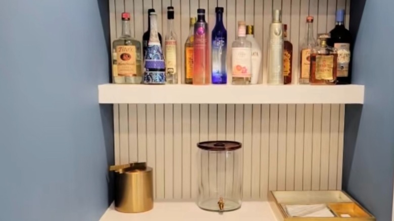 Bar drinks on a floating shelf with beverage containers on lower shelf