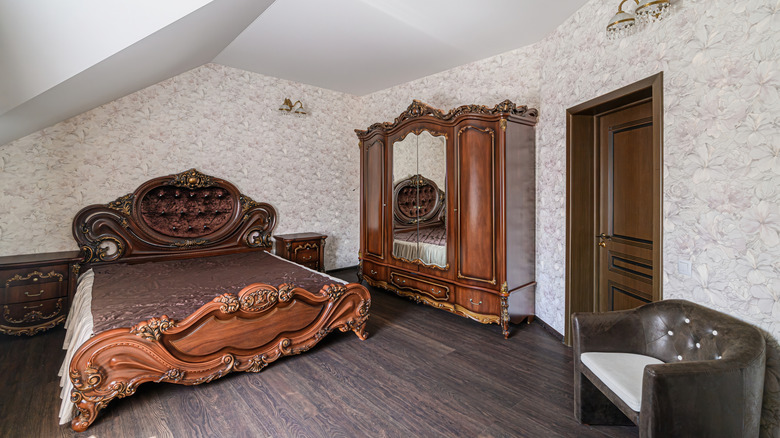 A bedroom with a large dark mirrored wardrobe and ornate darok wood bed. Patterned wallpaper is on the walls.