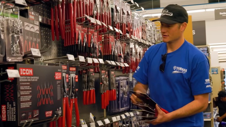 A young man in a baseball cap holds some Icon tools in his hand while shopping at Harbor Freight.