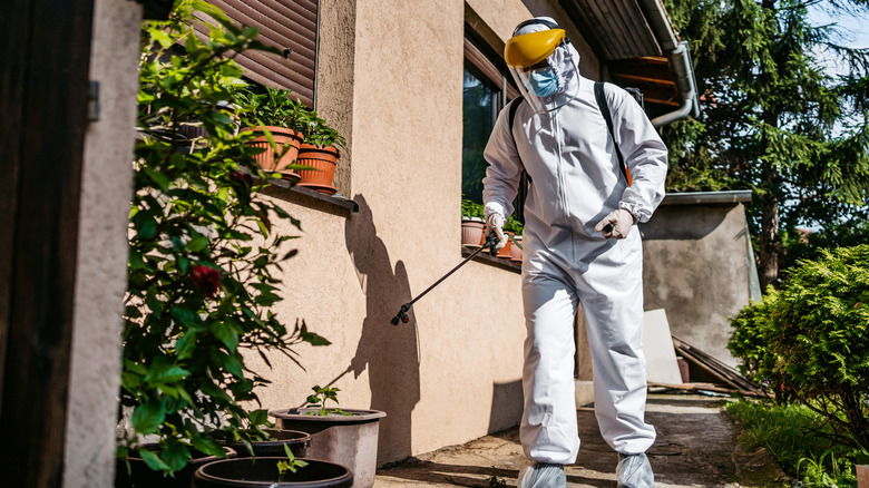 A person in full gear spraying the outside of a home