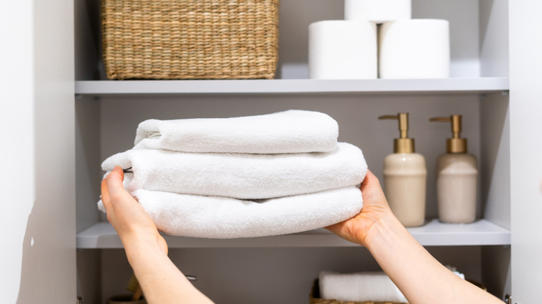 person putting clean towels in linen closet