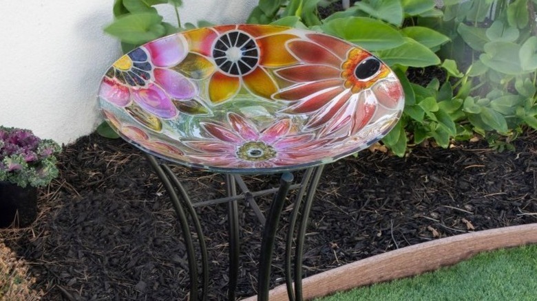 The Alpine bird bath bowl on a metal stand next to a garden bed