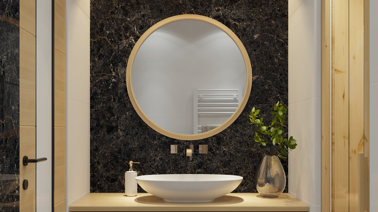 A bathroom with a round mirror featured
