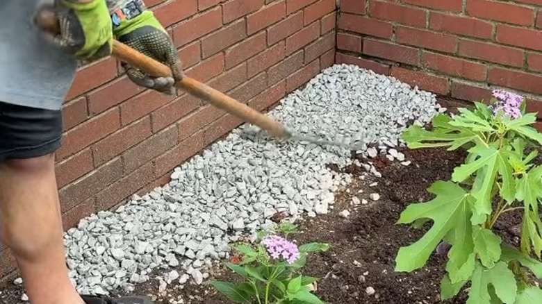A screenshot showing someone raking rocks into a path alongside the edge of their home