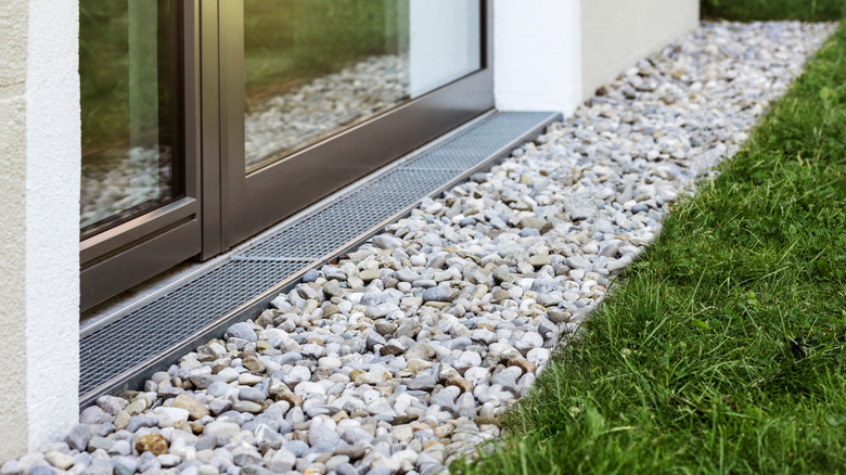 A drain path near a home with a sliding glass door on one side and green grass on the other