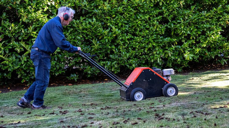 Person wearing ear protection pushes a core aerator in the yard