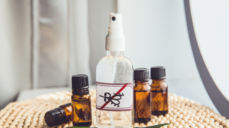 A DIY spray bottle meant to repel mosquitos sits on a table surrounded by essential oil bottls