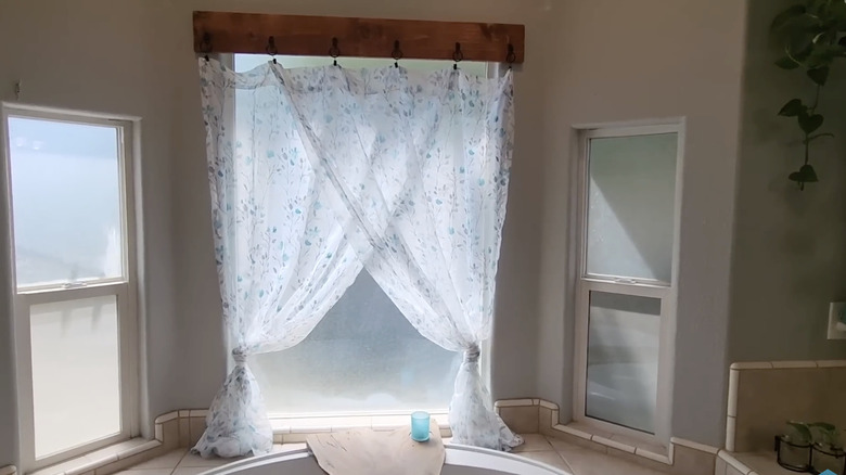 Curtains hang from a wooden plank with hooks in a bathroom.