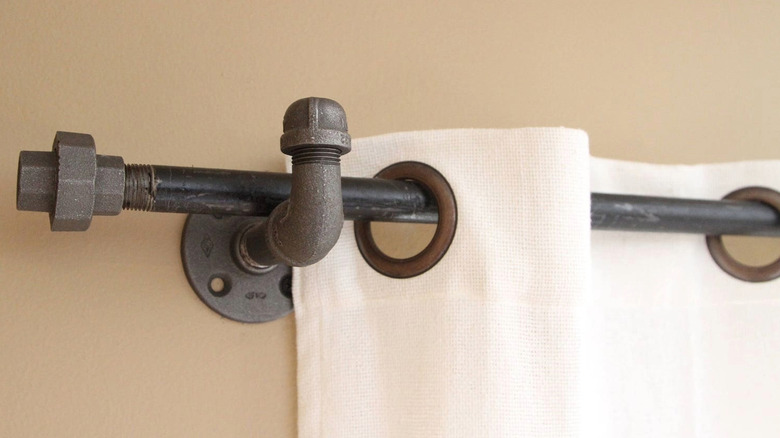White linen curtains hang from a curtain rod made from metal plumbing pipes.