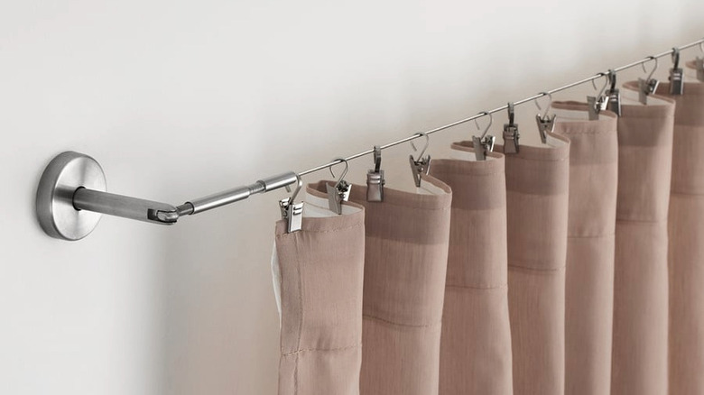 Beige curtains hang from clips attached to a curtain wire in a home.