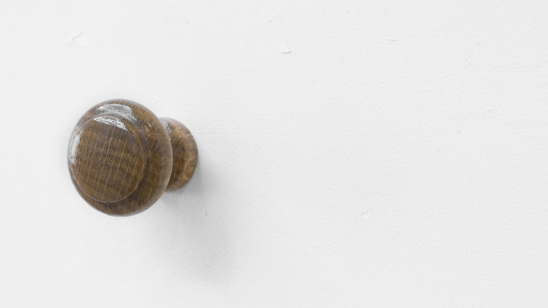 A wooden cabinet door knob mounted to a wall.