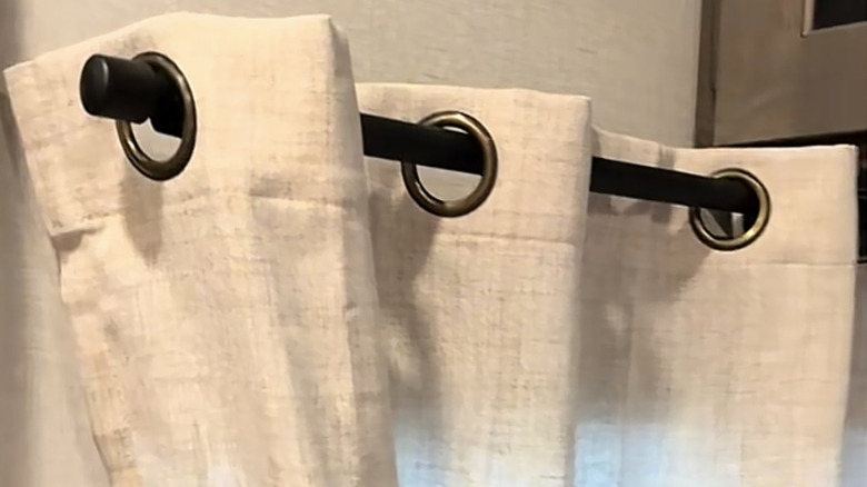 A cream curtain with large eyelets hangs from a PVC pipe.