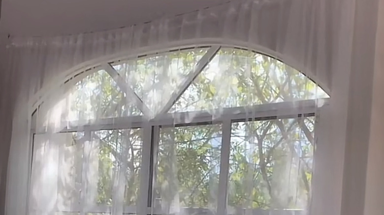 A sheer curtain hangs from a length of rope in front of a bay window.