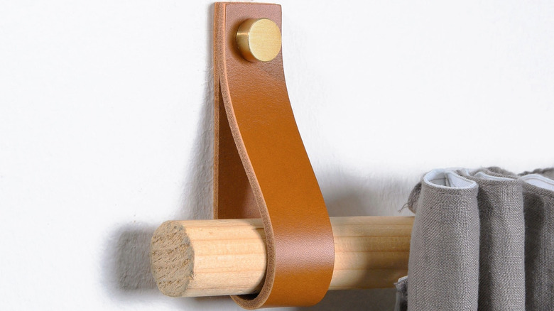 A wall-mounted leather strap holds a wooden dowel with a gray curtain hanging off it.