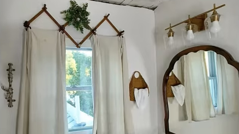 White curtains hang from a wooden accordion rack in a bedroom.