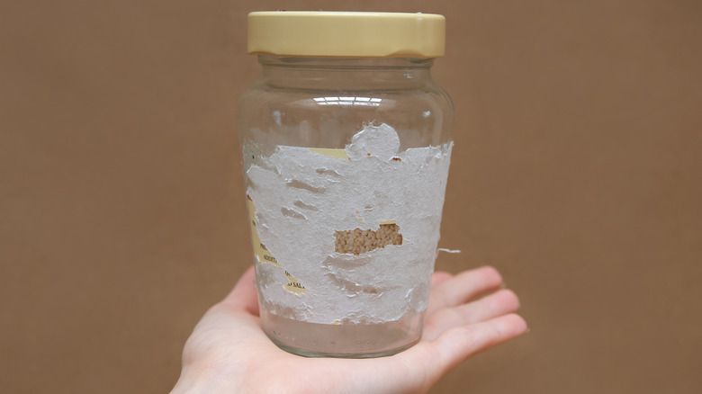 hand holding glass jar with sticker residue on it