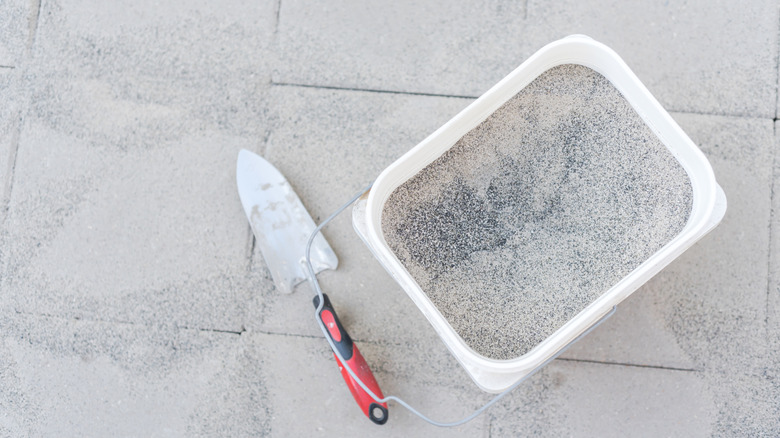 Bucket of polymeric sand on paver surface with trowel