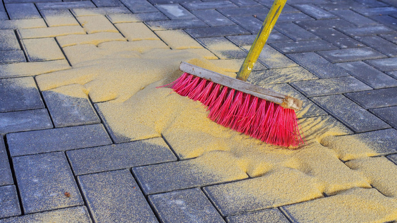 Broom sweeping sand into cracks between pavers