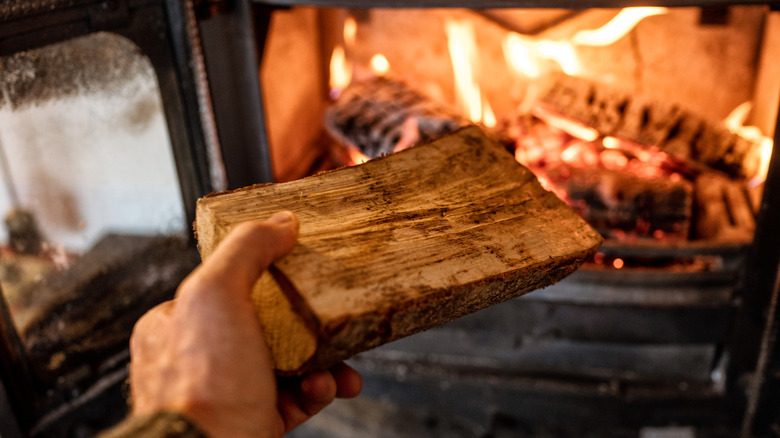 Hand putting chopped wood in a burning fireplace