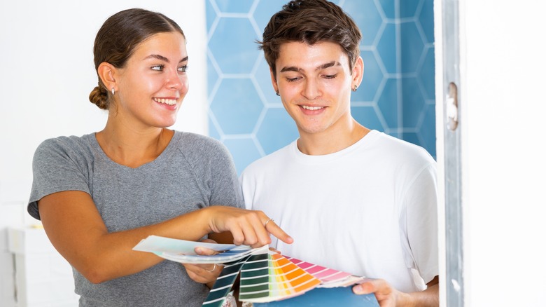 Young woman and young man looking at color swatches while holding a tile