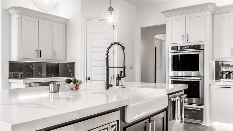 Modern kitchen with stainless steel appliances, white counters, white walls, and white cabinets