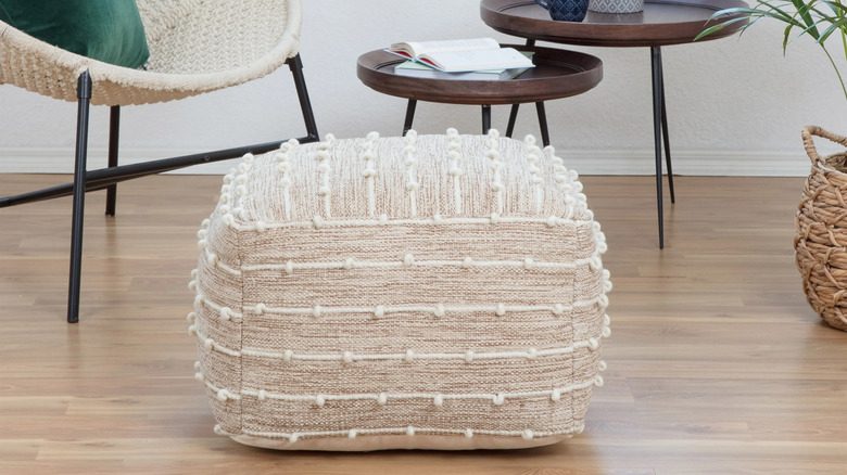 A light red pouf is placed on the floor in a bedroom next to a white cabinet and planters