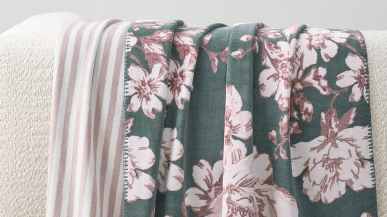 A pink floral reversible throw is draped on a bed