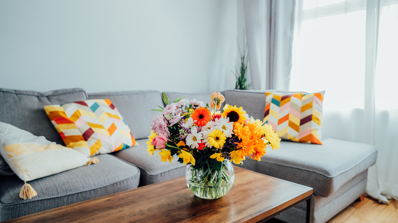 Brightly colored pillows adorn a couch while a vase filled with flowers sits on a table