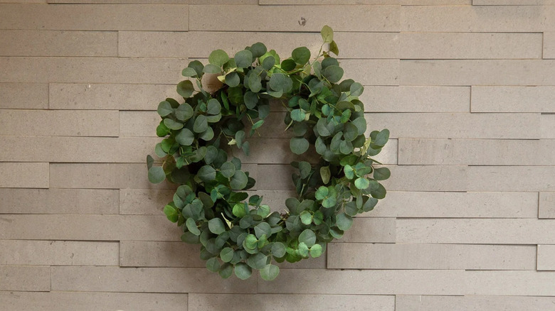 A faux eucalyptus wreath is hung on a light brick wall