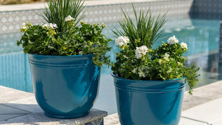 Two teal planters sit on an outdoor tiled surface, each containing arrangements of plants and flowers