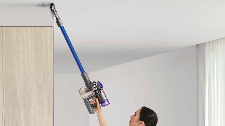 A woman is using a cordless vacuum to clean a ceiling