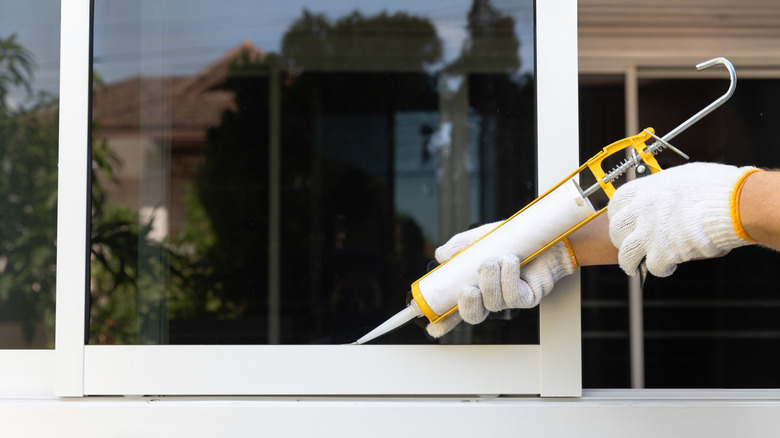A person runs a bead of caulk along a window to seal it