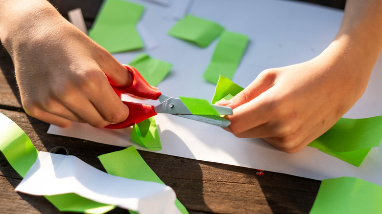 Person's hands cutting green and white paper