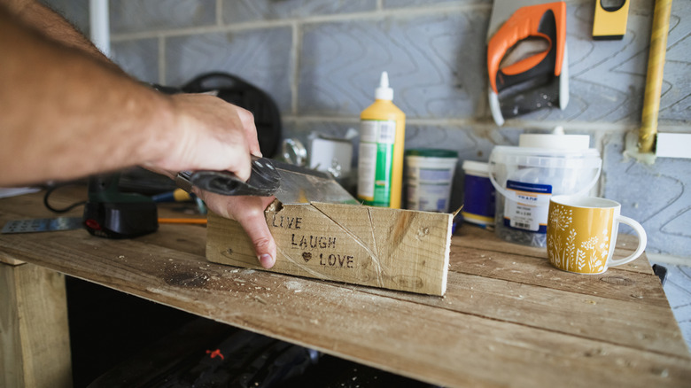 Person cutting wood plank with saw