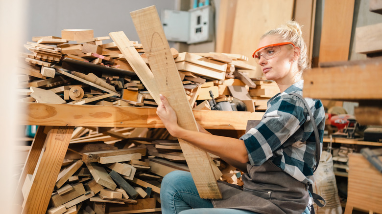 A woman with safety glasses holds pieces of scrap wood