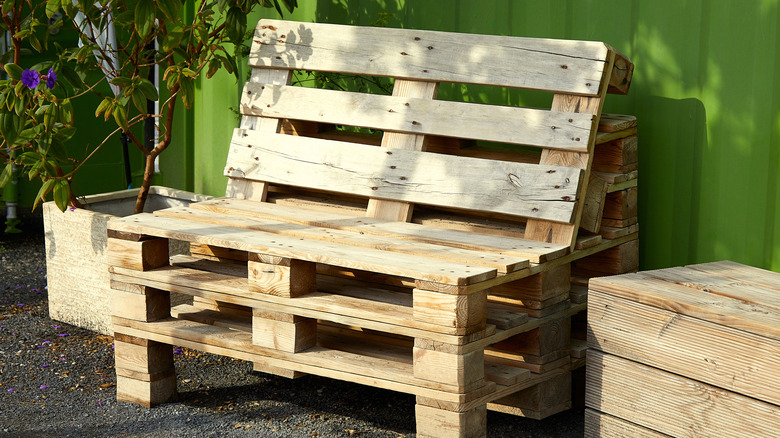Wooden pallet bench next to a green fence or shed