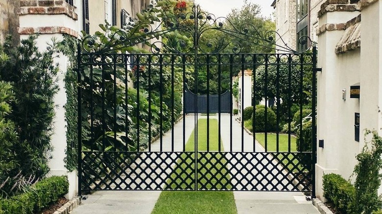 A grass strip driveway within a gate in an area with plants and shrubs