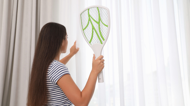 Women standing in front of a curtained window holding a fly swatter