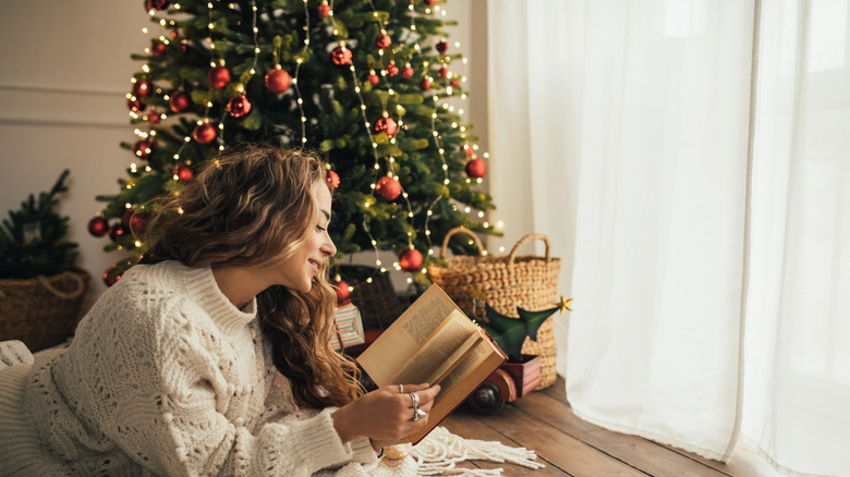 young woman reading book, lying on floor near Christmas tree