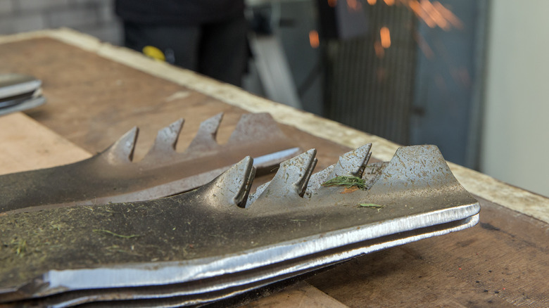 A close-up of mower blades with someone using a grinding wheel in the background